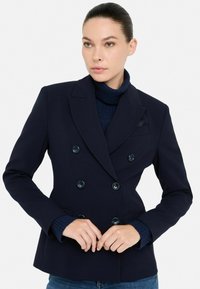 Námornícky dvojradový blazer s veľkými gombíkmi, klopovými goliermi a dvoma prednými vreckami. Pod ním je viditeľný štruktúrovaný rolák.
