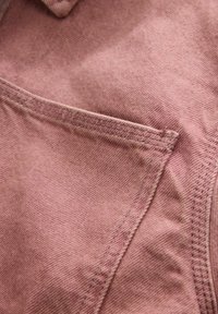 Gros plan sur une poche en tissu rose pâle délavé avec double surpiqûre et détails de couture sur un matériau en coton texturé.