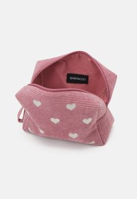 Pochette en velours côtelé rose avec des motifs en forme de cœur blancs, fermeture éclair et doublure en tissu. Comprend une étiquette intérieure avec le nom de la marque even&odd.
