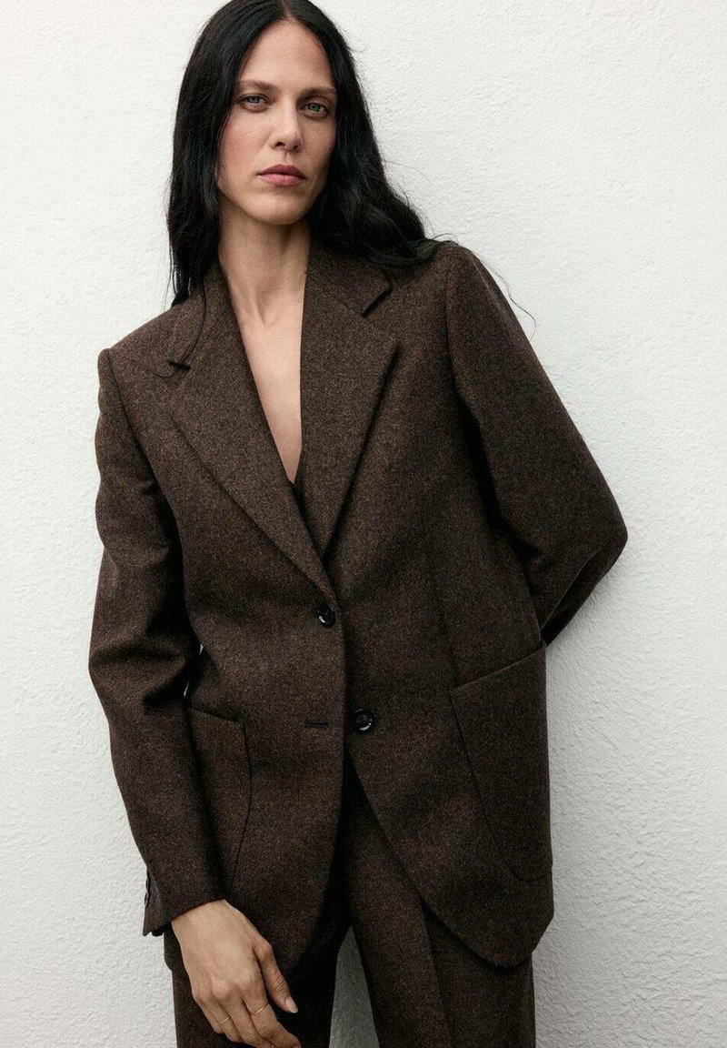 Blazer marrone in misto lana con spalle strutturate, rever a punta, due tasche frontali e bottoni neri. Tessuto liscio con vestibilità sartoriale.