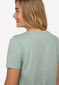 Camiseta de manga corta verde claro hecha de tela suave, con escote redondo y una costura en contraste en la parte posterior.