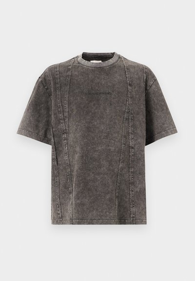 T-shirt cinza, oversized, de mangas curtas, feito de tecido texturizado; apresenta detalhes de costura em contraste e um logo sutil na parte da frente.