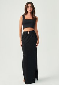 Melnas divdaļīgas apģērbs, kas sastāv no īsās blūzes ar platām siksnām un grīdas garuma svārkiem ar pēdas detaļu un rāvējslēdzēja akcentu.