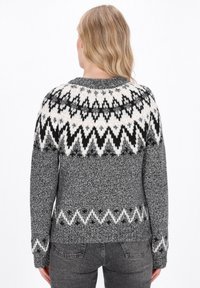 Grauer Pullover mit einem gemusterten Schulterbereich in Weiß und Schwarz, der Zickzackmuster aufweist. Stricktextur mit langen Ärmeln und einem runden Ausschnitt.