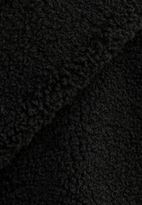 Primer plano de un suave y texturizado tejido de forro polar negro con una costura doblada visible en la parte superior derecha.