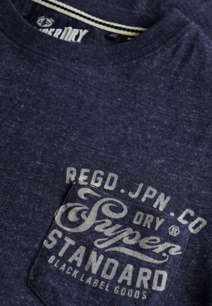 Navy blauwe t-shirt van textuurstof, met een borstzak met lichtgrijze merknaam en logo-tekst. Geribbelde hals met streep.