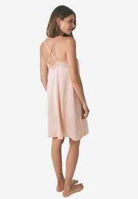 Lys pink satin slip kjole med blonder, justerbare tynde stropper og en flydende silhuet. Ryggen har et krydsende stropdesign.