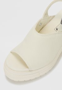 Chaussure slip-on en toile de couleur blanc cassé, dotée d'un design à bout ouvert, d'un talon rond et d'accents cousus. Semelle en caoutchouc texturée pour une meilleure adhérence.