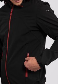 Zwarte softshell jas met rode ritsen en accenten, ritszakken, een hoge kraag en een slanke, getailleerde pasvorm. Glad oppervlak.