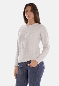 Maglione grigio chiaro a maglia, con collo rotondo classico, pattern testurizzato e polsini a costine, abbinato a jeans blu aderenti.