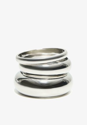 Trije zloženi sijoči srebrni kovinski obroči z gladkimi, zaobljenimi površinami na belem ozadju.