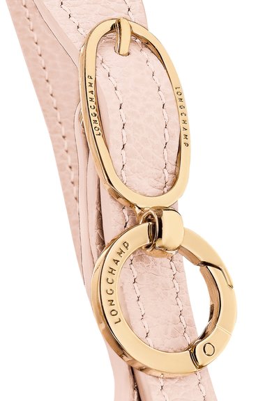 Light pink leather strap with gold hardware, featuring an oval and circular clasp with embossed "LONGCHAMP" branding. Smooth texture.