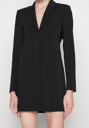 Zwart blazerjurkje van gestructureerde stof. Heeft een diep V-hals, lange mouwen en zijzakken. Getailleerde pasvorm met strakke lijnen.