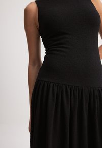 Svart klänning med en figurnära ärm-lös bodice och en strukturerad, veckad kjol, tillverkad av ett mjukt tyg med lätt stretch.
