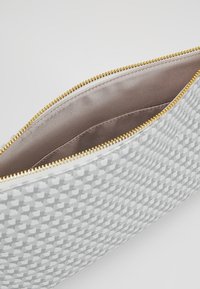 Trousse de maquillage gris à motif avec une surface lisse, fermeture éclair dorée et doublure en satin beige, présentant des motifs géométriques subtils.