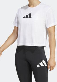 Camiseta blanca recortada con un logo negro, combinada con leggings negros con un detalle de logo blanco. Tela suave, mangas cortas, corte casual.