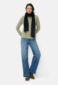 Stribet oliven- og cremefarvet langærmet top parret med blå flagrende jeans. Et mørkeblåt tørklæde omkring halsen. Olivengrønne ankelstøvler.