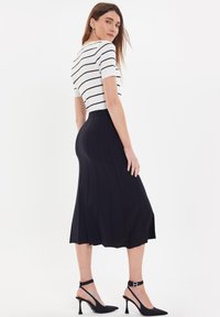 Gonna nera midi con dettagli di cucitura verticale, abbinata a una maglietta bianca a strisce a maniche corte. Modella che indossa tacchi neri a punta.