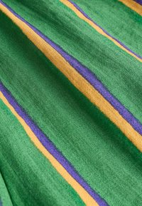 Grüner Stoff mit diagonal verlaufenden gelben und violetten Streifen, eingewoben in ein strukturiertes, weiches Material.