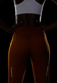 Athletikbekleidung aus formenden, atmungsaktiven Stoff in warmem Orange mit reflektierenden Akzenten an den Seiten und einem hohen Hüftbund.