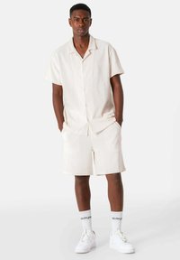 Lichtbeige overhemd met korte mouwen en een gestructureerd patroon, gecombineerd met bijpassende shorts. Draag het met witte sneakers en sokken met tekst.