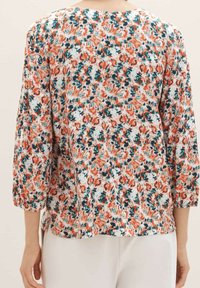 Blouse fleurie en tissu léger, avec des motifs orange, verts et bleus. Manches trois-quarts et encolure arrondie, avec des fentes sur les côtés.