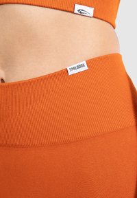 Reggiseno sportivo arancione a costine e leggings a vita alta con etichette SMILODOX. Presenta un tessuto testurizzato e un design senza cuciture per il massimo comfort.
