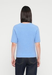 Maglione a maniche corte in maglia blu, con una texture morbida e soffice, colletto e orlo a coste, indossato con jeans in denim scuri.