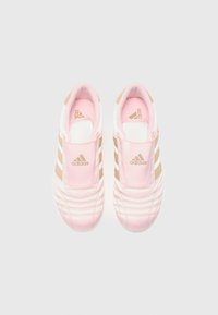 Sapatilhas cor-de-rosa claro com detalhes em dourado, apresentando um design tipo slip-on, três riscas brancas laterais e uma textura acolchoada.