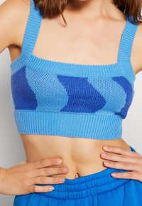 Modrý pletený krátký top s čtvercovým výstřihem, silnými ramínky a geometrickým vzorem v tmavě modré barvě. Měkká textura, přiléhavý design.