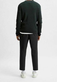 Mörkgrön texturerad tröja, svarta byxor och vita sneakers. Fokusera på minimalistisk design och skräddarsydd passform, sedd bakifrån.