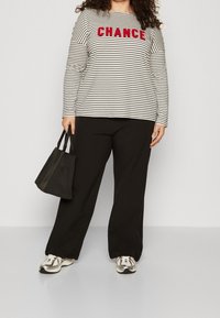 Striped long-sleeve shirt in white and black with red "CHANCE" text, paired with black wide-leg pants and silver-accented sneakers. Black handbag.