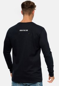Camiseta negra de manga larga con el texto en la parte posterior "LLEVA EL CÓDIGO". Confeccionada con un tejido suave y de textura lisa, y un diseño ajustado.