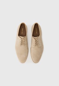 Beige suede shoes with a rounded toe, lace-up design, and smooth texture. Features a minimalist style and a light-colored sole.