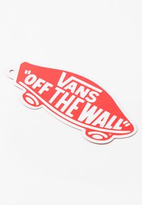 Vans "Off the Wall" logo etikett i rødt og hvitt, formet som en bil med bold skrift og blank finish. Inkluderer et hull for feste.