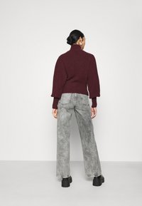 Pull en tricot bordeaux avec un col montant et des manches froncées, associé à un jean large taille haute gris clair et des bottes à plateforme noires.