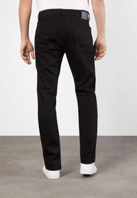 Pantalons en denim noir avec une coupe droite, dotés de deux poches arrière avec des coutures en zigzag, portés avec des baskets blanches.
