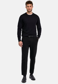 Maglione nero a maglia con colletto rotondo, abbinato a pantaloni neri su misura con cuciture strutturate, indossato con scarpe nere e una cintura.