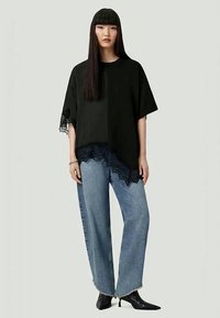 Black oversized t-shirt with lace trim, paired with light blue wide-leg jeans. Smooth texture, relaxed fit, contrasting lace detail at hem.