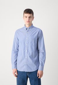 Blue and white striped button-up shirt with a collar, featuring a chest pocket and long sleeves. Worn with blue jeans.