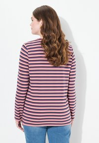 T-shirt à manches longues à rayures avec des rayures horizontales roses, bleu marine et blanches. Tissu doux avec un col rond, porté avec un jean bleu.