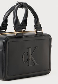 Čierna kožená kabelka s dvojitými hornými ušami, zlatým zipsom, embosovaným logom "cK" na prednej strane, obdĺžnikového tvaru, hladký povrch.