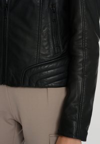 Zwarte leren jas met een slim fit ontwerp, textuur op het oppervlak en subtiele gewatteerde details op de schouders. Beschikt over ritssluiting zakken.