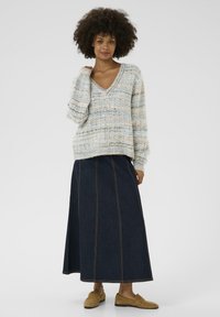 Paksu neulepaita kerman, sinisen ja beigehtävän sävyissä; V-aukko ja pitkät hihat. Yhdistetty pitkän tumma denimpitkän hameen ja ruskeiden loafer-kenkien kanssa.