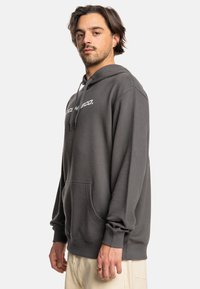 Gray hooded sweatshirt made of soft fabric, featuring a front pocket and drawstrings. Has a logo printed in white across the chest.