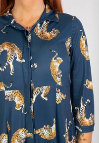 Navyblaues Kleid mit einem Button-Down-Kragen, das ein sich wiederholendes Muster aus orangefarbenen und weißen Tigern zeigt, aus einem glatten, leichten Stoff gefertigt.