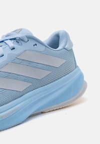 Chaussure de sport bleu clair avec une tige en maille, trois bandes grises, un col rembourré et une semelle en caoutchouc ronde. Convient pour les activités sportives.