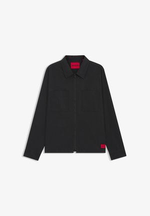 Zwarte jas met rits en kraag, twee borstzakken aan de voorkant, en rode "HUGO" labels op het binnenlabel en de onderzoom.