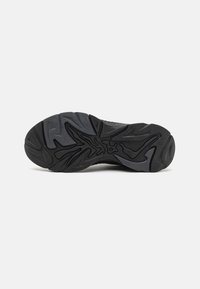 Black sneaker outsole with a textured surface, featuring a wavy, geometric pattern for grip. Durable rubber material, rounded toe design.