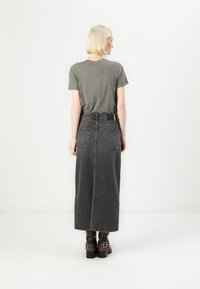 Grey T-shirt with rolled sleeves, paired with a long black denim skirt featuring pockets and a brown belt. Clear stitching details.